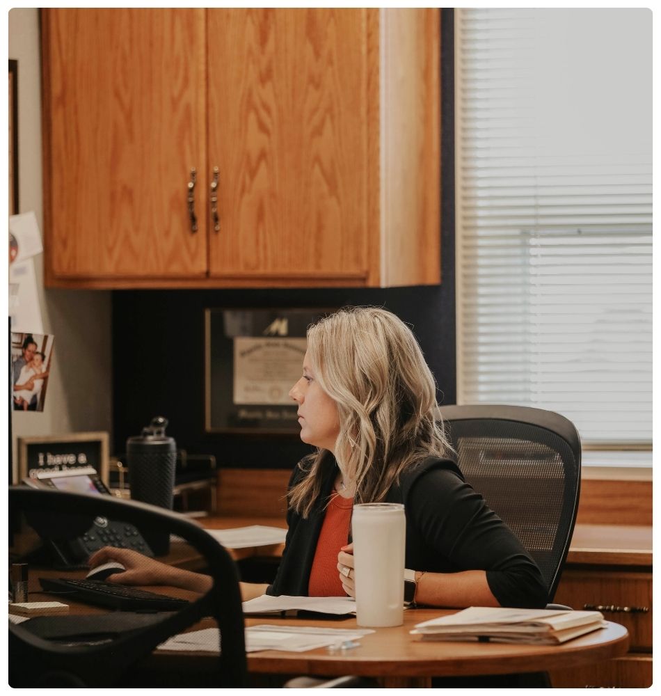 Woman working at a desk in an office with papers and computer keyboard.
