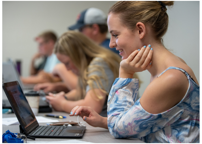 Student working on a computer in class alongside other Lake Region State College students.