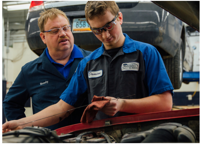 Instructor guiding a student during hands-on training in an automotive technology program.