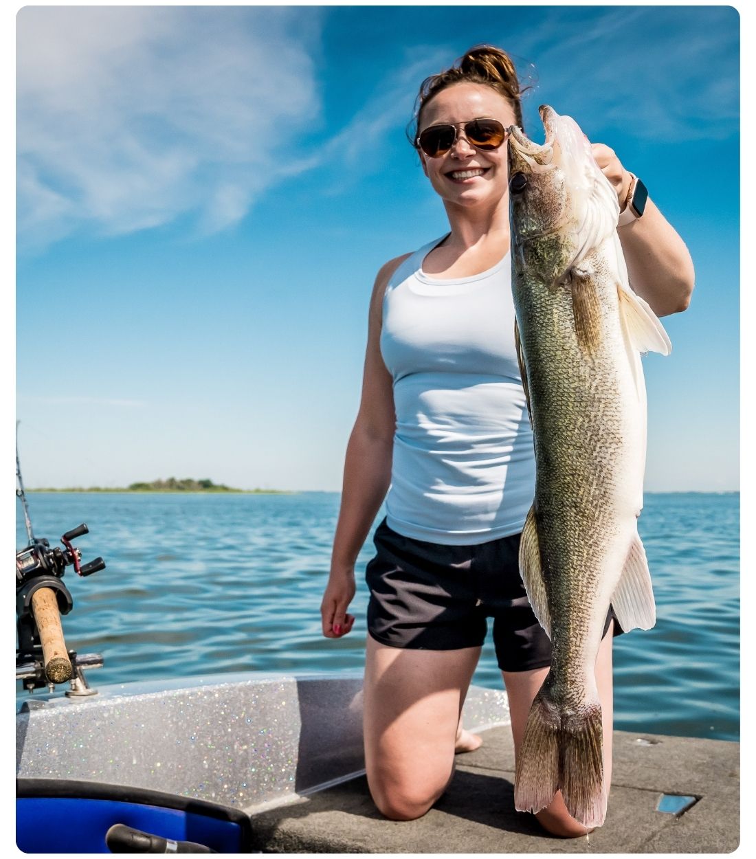 Girl kneeling on a boat holding a large fish on Devils Lake with open water and sky in the background.