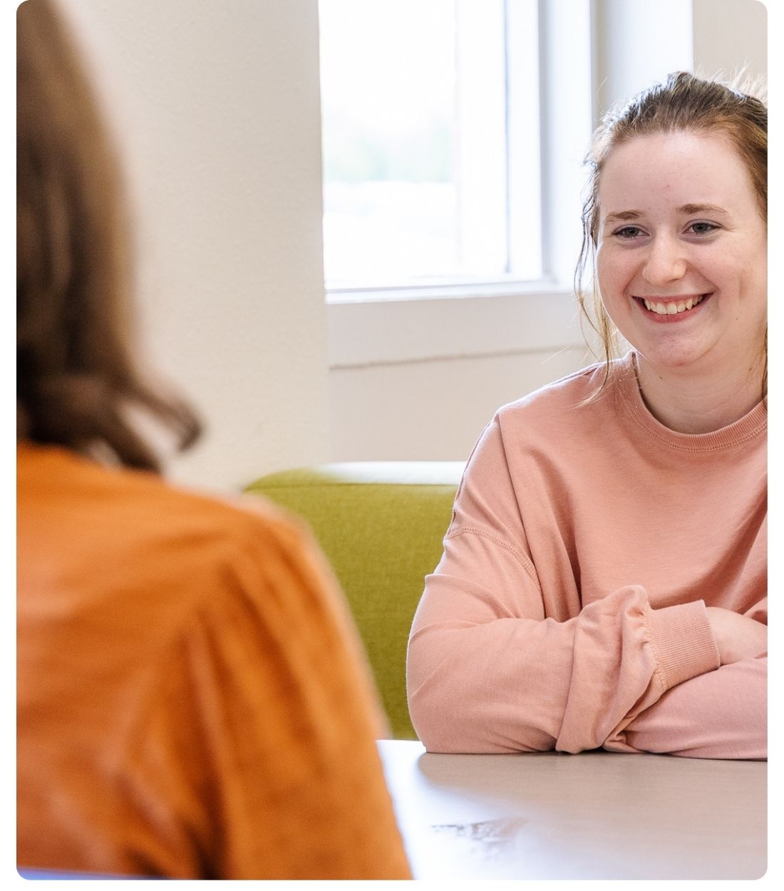 Lake Region State College student seated at a table, listening and engaging in conversation with another person in an indoor campus setting.