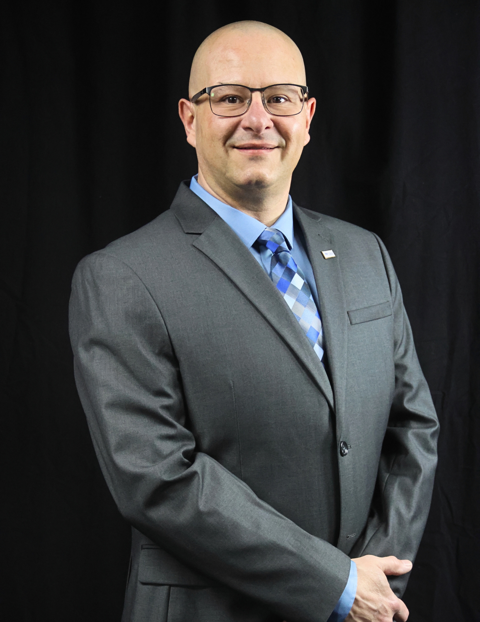Professional headshot of John Maritato wearing a gray suit, blue shirt, and tie, photographed against a black background.
