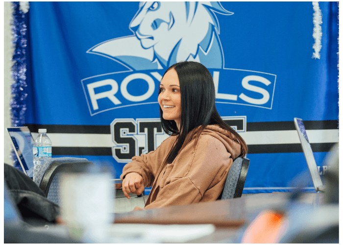 Student sitting in a classroom with a Lake Region State College Royals flag displayed on the wall behind her.