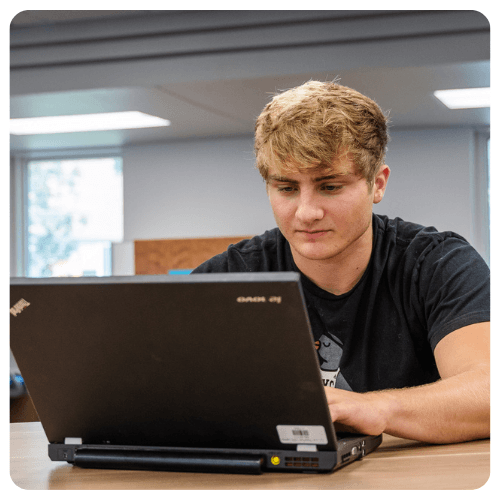 Lake Region State College student works on a laptop computer at a table inside a campus learning space.