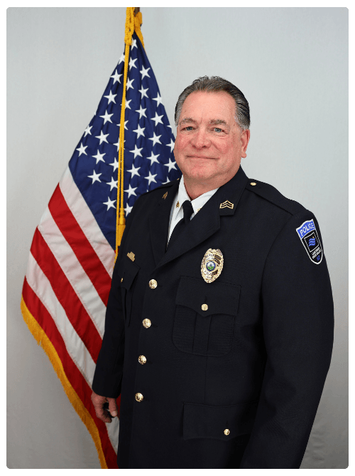Sgt. Greg LaHaise pictured indoors in front of an American flag, wearing a black uniform.