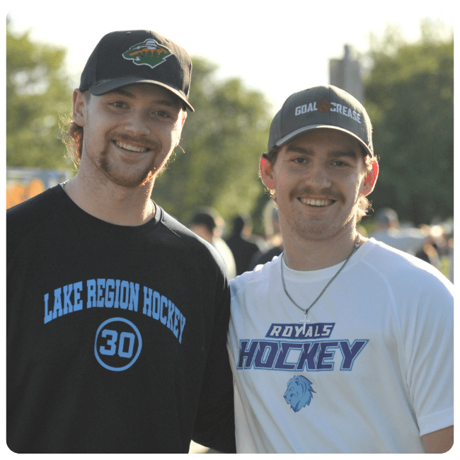 Two people standing outdoors wearing Lake Region Hockey and Royals Hockey apparel.