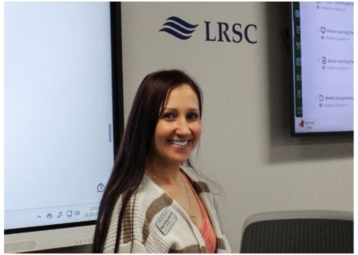 A person stands in a classroom next to an LRSC screen and a monitor displaying course content.