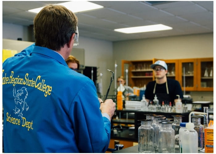 Science instructor demonstrating laboratory equipment to students in a classroom lab.