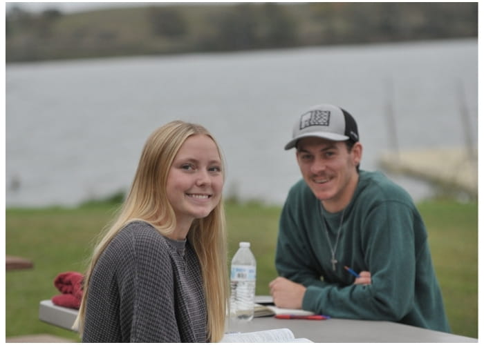 Two students reading outside near a lake.