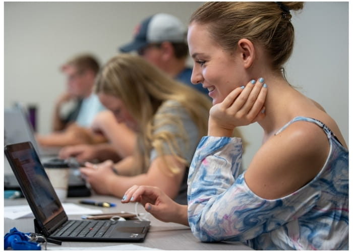 Student working on a computer in class alongside other Lake Region State College students.