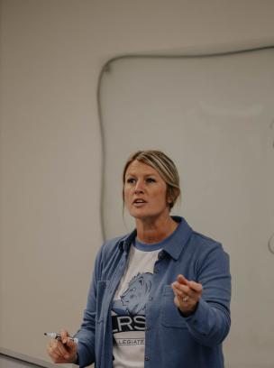 woman in blue sweater with blonde hair teaching.