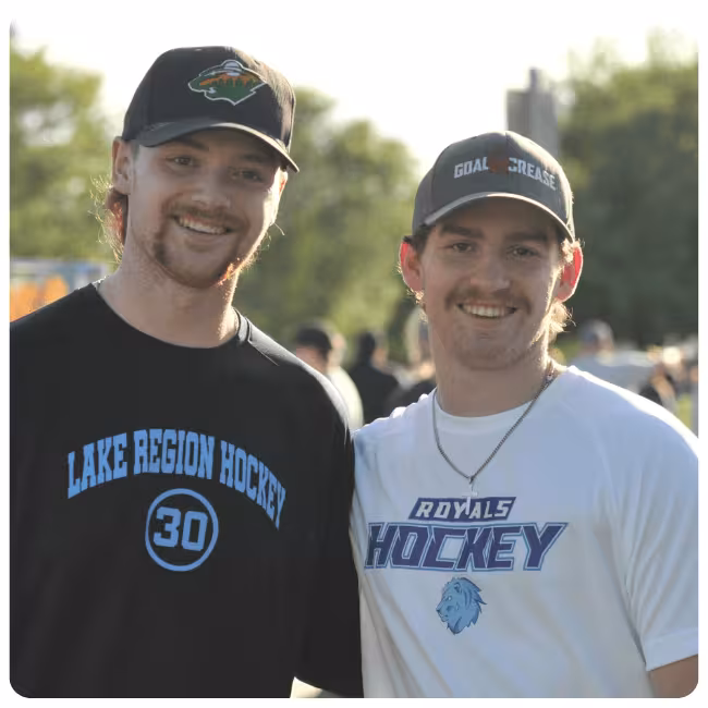 Two people standing outdoors wearing Lake Region Hockey and Royals Hockey apparel.
