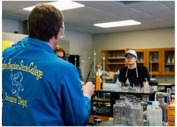 Science instructor demonstrating laboratory equipment to students in a classroom lab.