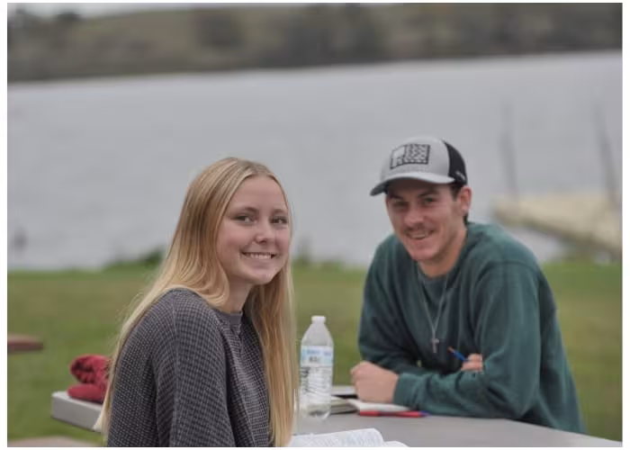 Two students reading outside near a lake.