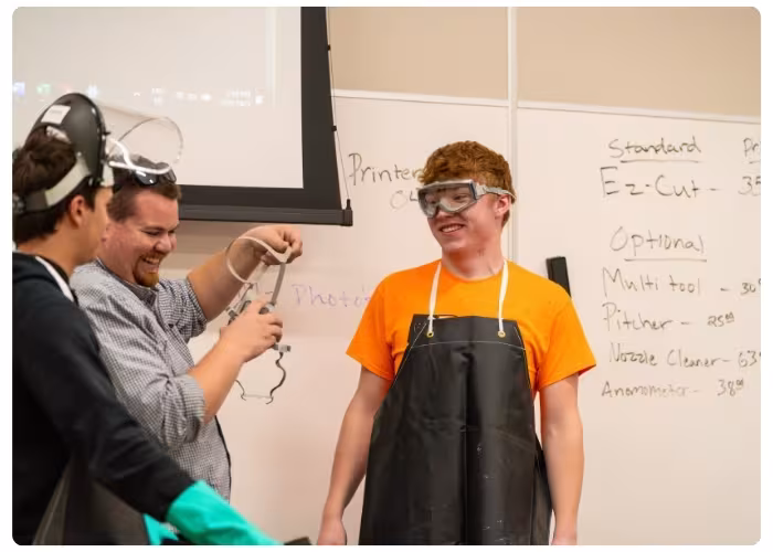 Students wearing safety goggles and protective gear participate in a hands-on lab activity in a classroom.