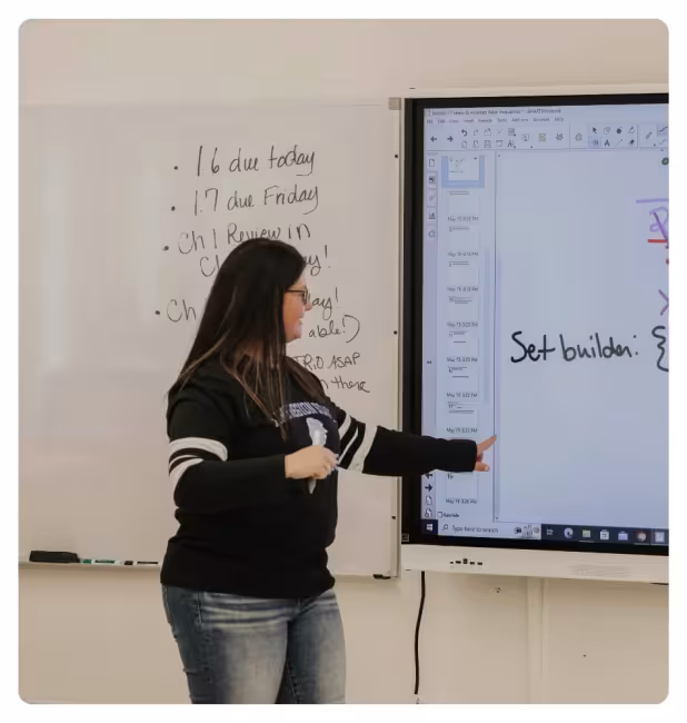 Instructor teaching at the front of a classroom using an interactive display and whiteboard.