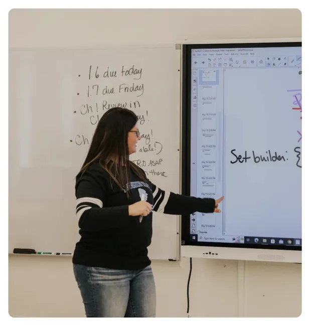 Instructor teaching at the front of a classroom using an interactive display and whiteboard.