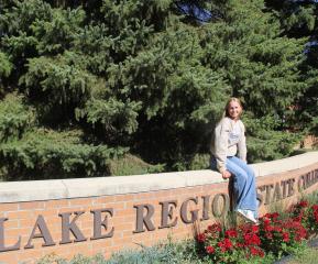 LRSC graduate Kassidy Hart sits on the LRSC brick sign in the front entrance.