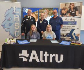 Two Red River students sit at the table to sign on with Altru as representatives of LRSC, Red River, and Altru look on