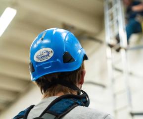 A wind energy student in safety gear watching classmate climb