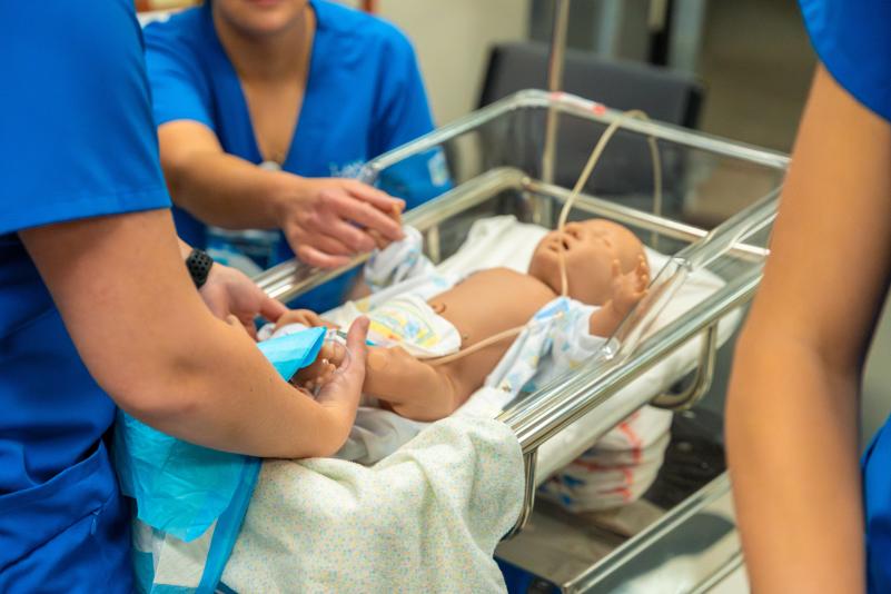 Three LRSC nursing students work on an infant mannequin in lab