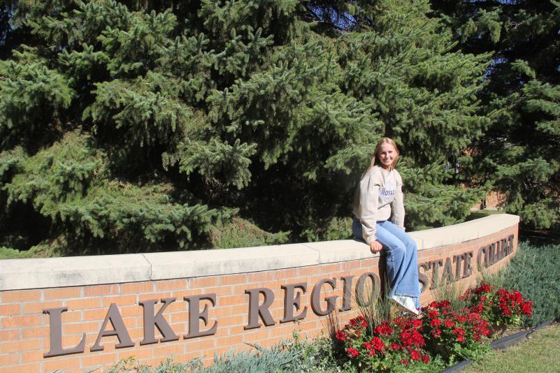 LRSC graduate Kassidy Hart sits on the LRSC brick sign in the front entrance.
