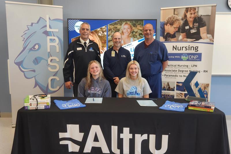 Two Red River students sit at the table to sign on with Altru as representatives of LRSC, Red River, and Altru look on