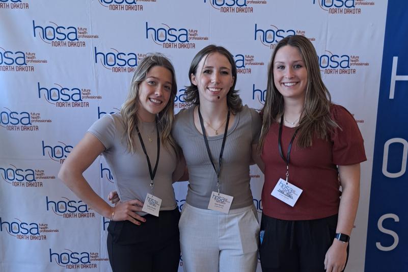 Sydney, Keira, and Sadie standing in front of HOSA screen