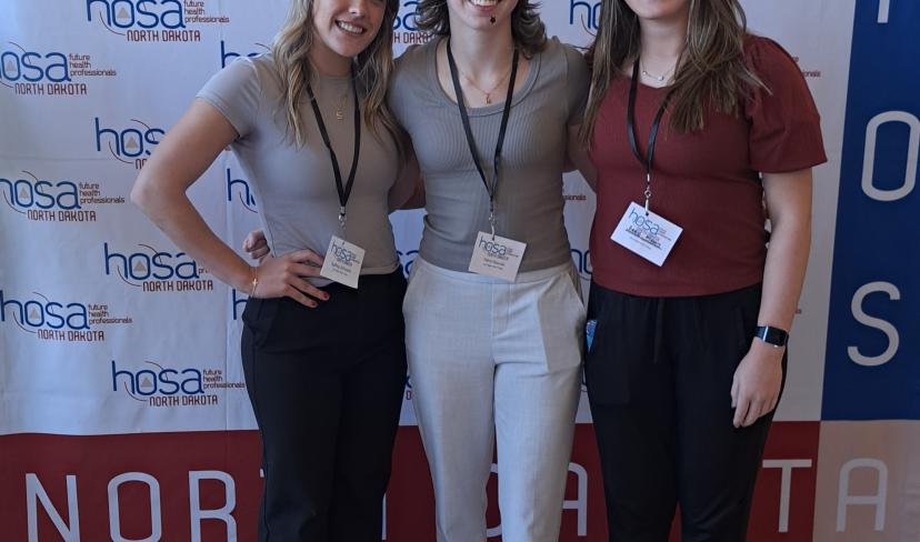 Sydney, Keira, and Sadie standing in front of HOSA screen
